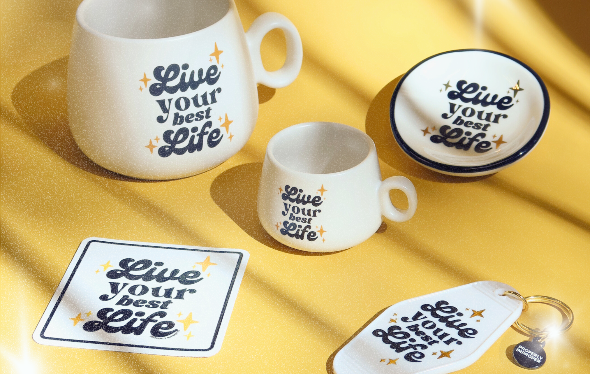Mugs, coasters, and keychains with 'Live your best life' text on a yellow fabric background